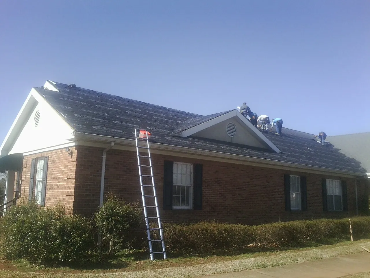 Crew tearing shingles off a brick ranch roof with a ladder set — Metal Roof Repair work by our crew in Springtown