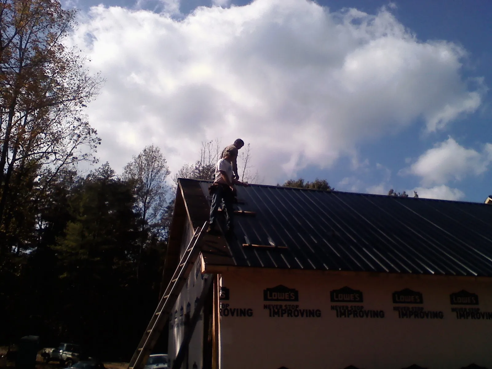 Roofer fastening dark metal panels high against a cloudy sky, from a Roof Inspection job in Springtown